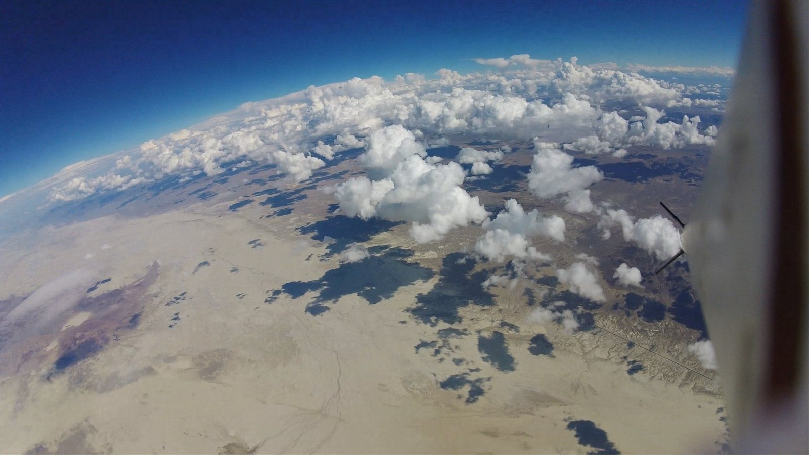 A view from a rocket in flight, looking down over clouds and desert terrain