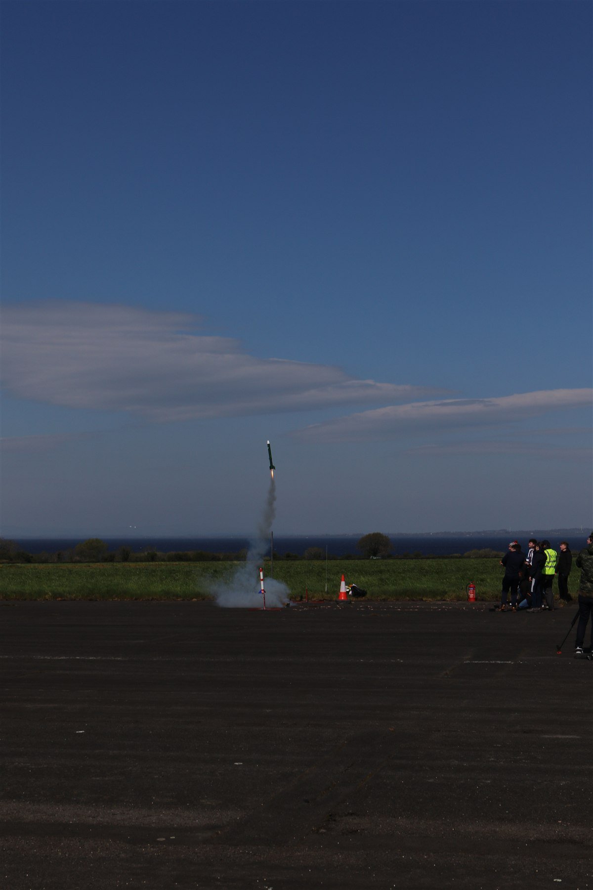A rocket lifting off with a visible exhaust plume as the launch team watches from the ground