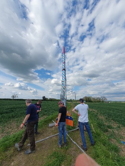 Team members preparing a tall, colourful rocket on its launch rail in a field