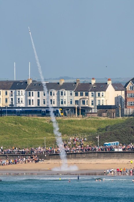 A rocket climbing above the beach and spectators at Portrush, leaving a trail of smoke