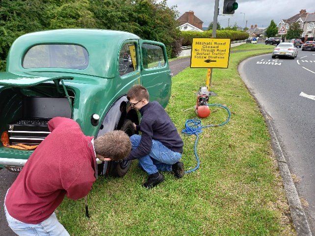 Two people changing a wheel on a green Morris 8 beside the road
